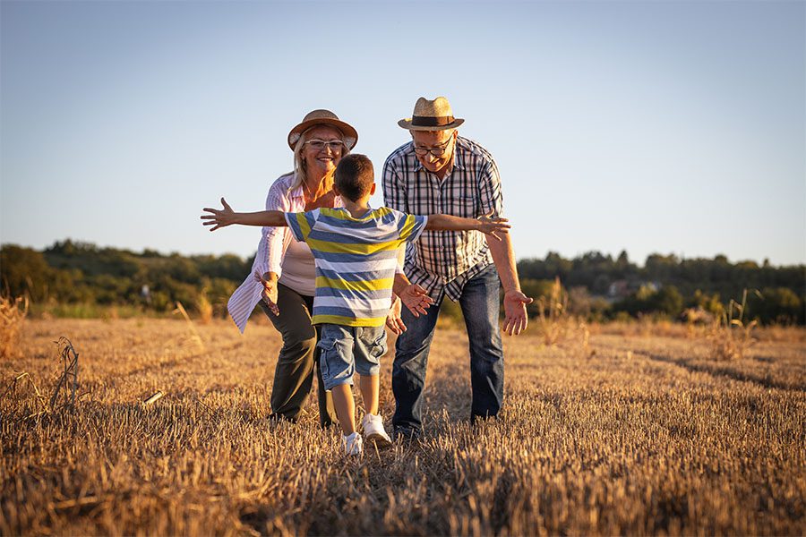 About Our Agency - View of a Young Boy Walking Up to His Grandparents While Holding His Arms Out for a Hug at Sunset on a Farm Field