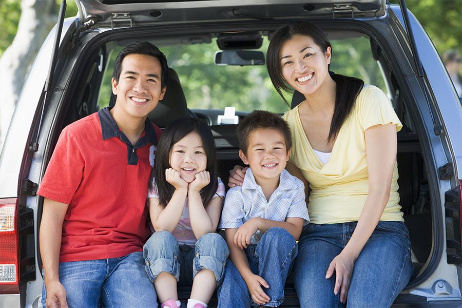 Blog - Portrait of a Cheerful Family with Two Young Kids Sitting in the Back Trunk of Their Car While Visiting the Park