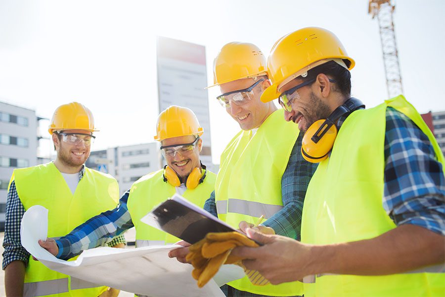 Specialized Business Insurance - Group of Smiling Contractors Standing Outside Looking at Blueprints and a Tablet to Plan Out Commercial Construction Project